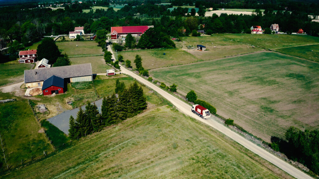 En flygbild över en lantlig by. En röd sopbil ses åka längs en väg.