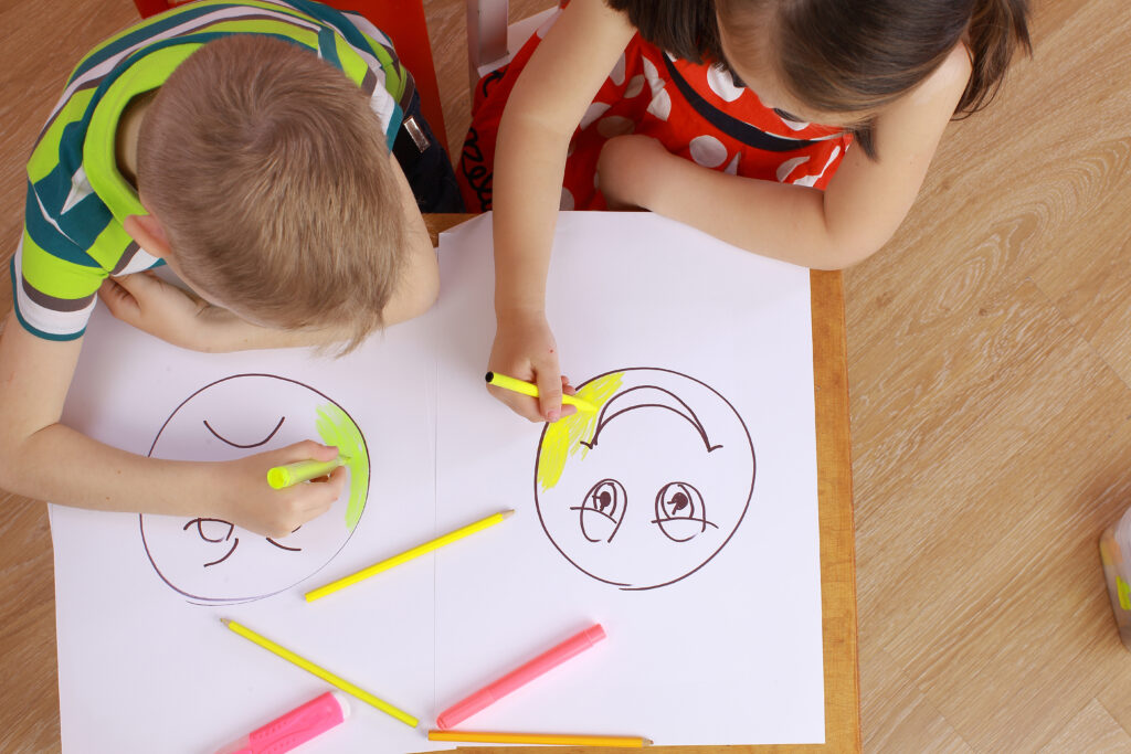 Två barn ritar en ledsen och en glad gubbe.