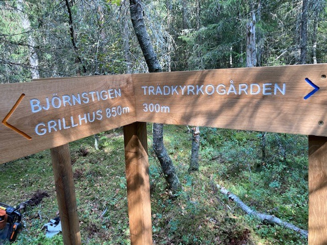 Träskyltar med pilar placerade i skogen. På den ena står det Björnstigen Grillgus 850 m och på den andra Trädkyrkogården 300 m