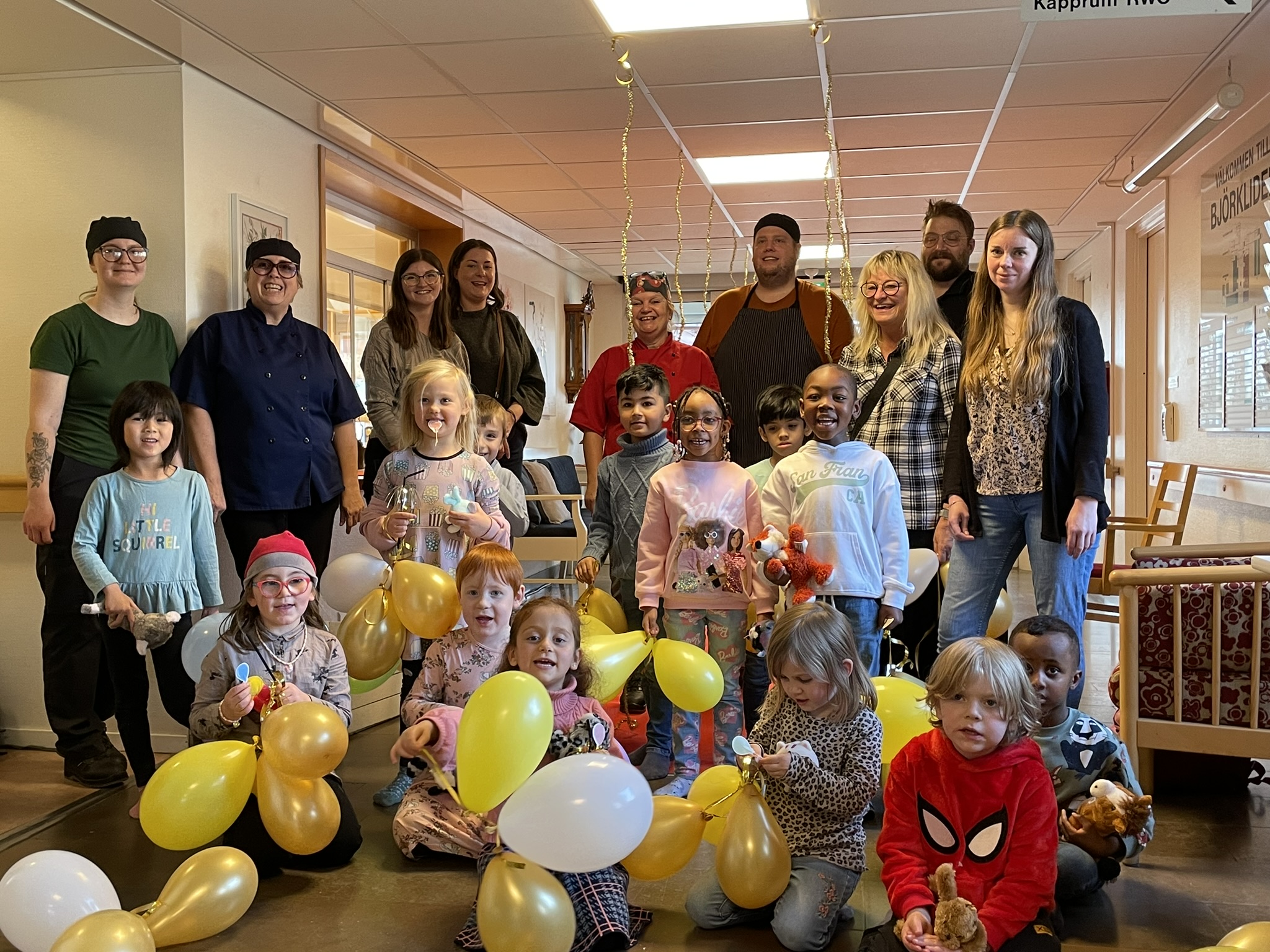 En stor grupp med barn och vuxna. Barnen håller i ballonger