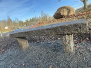 Vilobänk utformad av tre större stenblock. Bussterminalen skymtas i bakgrunden.