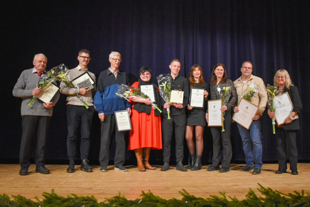 Nio personer står på rap på en scen. De har diplom och blommor i händerna