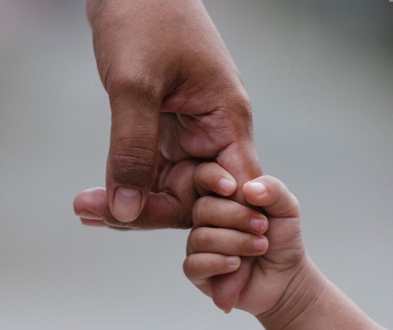 Närbild på barnhand som håller hårt i en vuxenhands pekfinger.